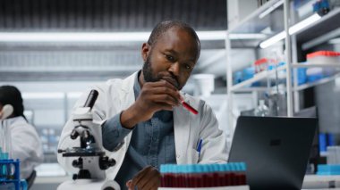 Laboratuvarda hematoloji uzmanı. Laptop yazılımı kullanarak test tüpündeki kan örneklerine bakıyor. Epidemiyoloji uzmanı, B kamerasındaki sanguin sıvısı örneğini analiz etmek için dizüstü bilgisayar programı kullanıyor.