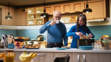 Emekli çift tost makinesinden tost makinesiyle kahvaltı hazırlıyor, tezgahın yanında yan yana duruyorlar. Kadın ve erkek bir anın tadını çıkarıyorlar. Emeklilik hayatı boyunca sohbet edip kaynaşıyorlar. Kamera A.