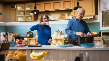 Yaşlı karı koca, hafta sonlarını modern mutfakta kahve ve tostla sağlıklı kahvaltı hazırlamakla geçirirler. Emeklilik çağında neşeli bir bağ ve rahatlatıcı bir yaşam tarzı. Kamera A.
