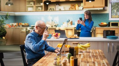 Apartman mutfağında akıllı telefondan kayan ve rahat ev işleri yapan yaşlı doğal kadın portresi. Yaşlı yetişkin, neşeli yaşam tarzını yansıtıyor ve emeklilikten memnun. Kamera A.