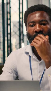 KPI ölçümlerini ve modern ofis çalışma alanındaki sezgilerini analiz eden Afrikalı Amerikalı iş adamının dikey video portresi. Görsel veriler, tahmin raporları, stratejik planlama ve küresel planlama için dizüstü bilgisayar kullanımı