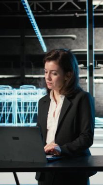 Dikey video veri merkezi kadın programcısı elektronik sorunları çözmek için dizüstü bilgisayar ve AR viralizasyonunu kullanır. VFX kompozitasyonu, sistem hatalarını düzeltmek için masadaki dizüstü bilgisayarı kullanan sunucu merkezi çalışanı