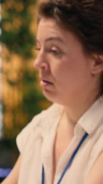 Dikey video aşırı çalışan kadın kronik yorgunluk ve tükenmişlik belirtileri gösteriyor, yüksek sorumluluk nedeniyle etkisiz ve tükenmiş. Modern şirkette masasında oturan yorgun ve bitkin bir kadın.