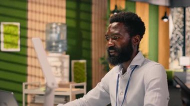 Siyahi erkek profesyonel modern ofiste görev yönetimi yapıyor, kontrol panellerini ve bilgisayardaki KPI görsel verilerini analiz ediyor. İstihbarat ve parasal görüşe sahip küresel iş amaçları.