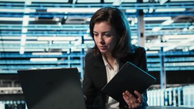 Veri merkezi yazılım geliştiricisi dijital ikiz simülasyonu için aygıtları kontrol paneli olarak kullanır. Mavi kablo ağ donanımı ayarlarını ayarlamak için laptop ve tablet kullanan sunucu merkezi kadın programcısı, kamera B