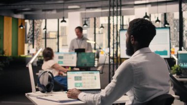 Afrikalı Amerikalı iş adamı, laptop 'da veri analizi, performans değerlendirmesi, modern kurumsal çalışma alanı. Stratejik hedefler ve verimlilik için grafikler, KPI gösterge paneli.