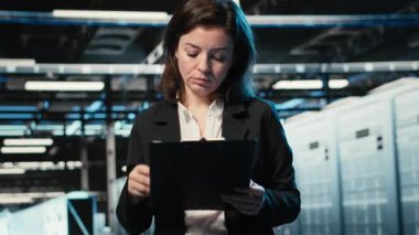 Altyapı durumu, dosya dosyaları ve holografik görsellerle veri merkezinde yönetici doğrulaması yapılıyor. Denetleme ekipmanları, kablo simülasyonu ve denetim çizelgeleri kullanarak sunucu odasında çalışan, kamera B