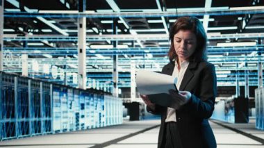 Veri merkezi yöneticisi altyapı durumunu pano dosyaları ve holografik görsellerle doğruladı. Sunucu odası çalışanı denetim çizelgeleri ve mavi kablo simülasyonu kullanarak ekipmanları denetliyor, kamera A