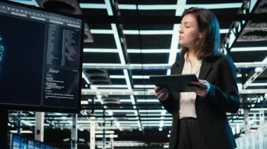 Veri merkezi programcısı tablet üzerinde kodlama yapıyor, dijital ikiz oluşturmak için ekipman donanımı tarıyor. Sunucu merkezindeki kadın teknisyen aygıt, VFX bileşimi, kamera A üzerinde programlama betiği çalıştırıyor