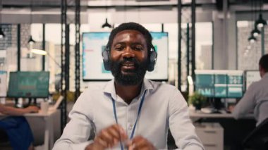 Rahat iş adamı, müzikten hoşlanan, ofiste kısa bir mola, kablosuz kulaklık, dizüstü bilgisayar ve grafikler, KPI ölçüm ve veri analizi, kurumsal bir ortamda birden fazla işi olan neşeli siyahi adam..