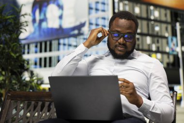 İnternet 'te bilgisayarla buluşan Afrikalı Amerikalı biri kulak kabuğu takıyor, günlük yaşam tarzını ve iş hayatını canlı şehir caddesinde harmanlıyor. Parktaki bankta video bağlantısı.