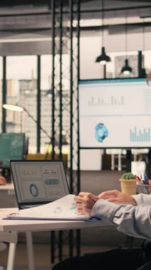 Vertical Video Professional çalışanı masadaki dizüstü bilgisayardaki uyum verilerini gözden geçirir, performans değerlendirmesini sağlar ve ofiste risk değerlendirmesi yapar. Ticari istihbarat desteği için görsel veri