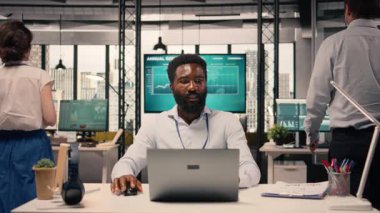 Siyahi bir adam, dizüstü bilgisayarda çalışan profesyonel, çok uluslu bir şirket, kurumsal ofis ortamı. İş zekası, tahmin raporları, üretkenlik, planlama ve kalkınma hedefleri.