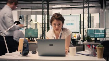 İş kadını müzik dinliyor, kablosuz kulaklık takıyor, modern ofiste çalışıyor. Kadın çalışanın dizüstü bilgisayarını kullanarak stres atışıyla üretkenliği birleştirdiği rahatlama anı..