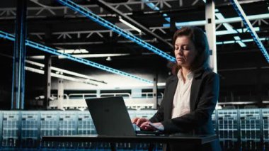 Veri merkezi yazılım geliştiricisi dizüstü bilgisayarla sunucu yükü dengelemeyi optimize ediyor. Sunucu çiftliğindeki kadın, verimliliği arttırmak için sistem parametrelerini ayarlıyor. Kamera A.