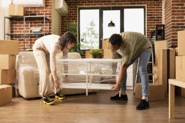 Afrika kökenli Amerikalı koca ve Kafkasyalı eş yeni tuğla duvar içinde kahve sehpası taşıyorlar. Çok ırklı evli çift taşınma gününde masa kaldırıyor ve rahat bir oturma odası hazırlıyor..