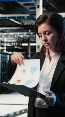 Dikey video okuma evrakları, mavi kablo örgüsü ve veri merkezindeki donanım donanımlarını denetleyen yönetici. Belgeler analiz ediliyor, AR altyapı görselleştirme ve sunucu çiftliğinde çalışan kadın, kamera A