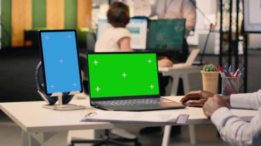 Dikey mavi ekran ve laptopta siyah adamla birlikte yeşil ekran, veri analizi ve iş istihbaratını inceliyor. Profesyonel ofis faaliyetleri, görsel veriler ve raporlar kaynak tahsisine yardımcı olur.