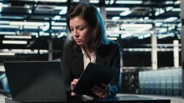 Veri merkezi yazılım geliştiricisi aygıtları kullanarak ekipman donanımlarını optimize ediyor. Sunucu çiftliğindeki kadın dizüstü bilgisayar ve tablette programlama betiği çalıştırıyor, sistem parametrelerini ayarlıyor, kamera B