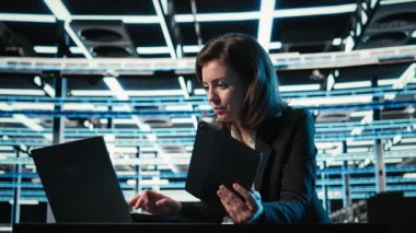 Veri merkezi yazılım geliştiricisi dijital ikiz simülasyonu için aygıtları kontrol paneli olarak kullanır. Mavi kablo ağ donanımı ayarlarını ayarlamak için laptop ve tablet kullanan sunucu merkezi kadın programcısı, kamera A