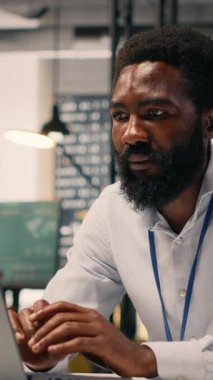 Örgütsel başarı için dizüstü bilgisayardaki görevleri çözen, KPI ve parasal verilerle performans değerlendirmesi yapan siyahi çalışanların dikey video portresi. Ofiste verimlilik ve kurumsal yaşam tarzı.