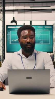 Dikey Video Siyah Adam, dizüstü bilgisayarda çalışan profesyonel, çok uluslu şirket, kurumsal ofis ortamı. İş zekası, tahmin raporları, üretkenlik, planlama ve kalkınma hedefleri