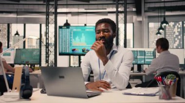 Afrika kökenli Amerikalı iş adamının portresi KPI ölçümlerini ve modern ofis çalışma alanındaki sezgileri analiz ediyor. Görsel veriler, tahmin raporları, stratejik planlama ve küresel işletme için dizüstü bilgisayar kullanımı.