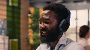 Afro-Amerikan adam kulaklıkla müzik dinliyor, bilgisayarla çalışıyor ve stres atışıyla odaklanmış iş analizini birleştiriyor. Ofisteki ses ve görevlerle birden fazla görev.