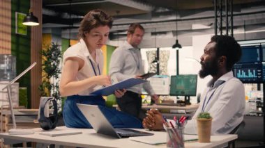 Modern kurumsal ofiste iş birliği yapan çeşitli iş adamları görsel verileri, grafikleri ve dizüstü bilgisayardaki KPI panellerini inceliyor. Performans ölçümlerini ve tahminleri tartışan profesyoneller.