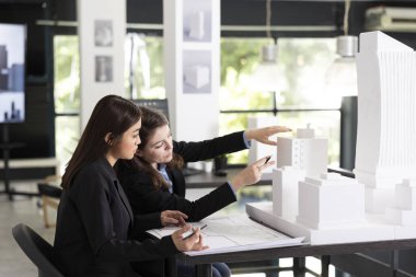 Odaklanmış kadın mimarlar modern ofiste beyaz mimari modelleri incelerken işbirliği yaparlar. Genç profesyoneller proje detaylarını gözden geçirir, yapı, planlama ve tasarım doğruluğunu tartışır.
