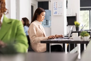 Çalışkan bayan çalışan masada oturuyor, çevrimiçi pazarlama raporlarını okuyor ve meslektaşlarıyla grup toplantısına hazırlanıyor. Asyalı kadın yönetici başlangıç ekibi için e- postaları kontrol ediyor ve günlük görevleri planlıyor.