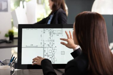 Kadın mimar dokunmatik ekranda ayrıntılı dijital kat planını gözden geçiriyor. Profesyonel tasarımcı yerleşim ölçümlerini değerlendirir ve gelecek proje için güncellenmiş mimari belgeleri hazırlar.