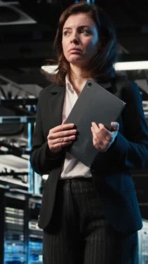 Dikey video otomasyonu, tablet ve mühendis veri merkezinde yürüyor, endüstriyel sistemleri izliyor. IT uzmanı sunucu odası IT profesyoneli ağ donanımı performansını denetlemek için aygıt kullanıyor