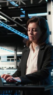 Dikey Veri Merkezi yazılım geliştiricisi laptop kullanarak sunucu yükünü dengelemeyi optimize ediyor. Sunucu çiftliğindeki kadın, verimliliği arttırmak için sistem parametrelerini ayarlıyor. Kamera A.