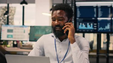Ofisteki cep telefonuyla konuşan siyahi profesyonel bir erkek. KPI için iş istihbaratını destekleyen dizüstü bilgisayardaki görsel veriler, grafikler ve grafikler, stratejik planlama.