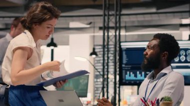 Modern kurumsal ofiste iş birliği yapan çeşitli iş adamları görsel verileri, grafikleri ve dizüstü bilgisayardaki KPI panellerini inceliyor. Performans ölçümlerini ve tahminleri tartışan profesyoneller.