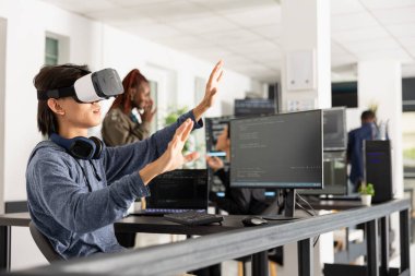 Erkek programcı VR gözlük kullanır, 3D arayüzle etkileşim kurar ve kodlama metinlerini analiz eder. Yenilikçi bir şirkette çalışan genç bir erkek yazılım geliştirme için sanal teknolojiyi keşfediyor..