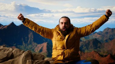 Zirvede duran kararlı dağcı huzurlu bir başarı anının tadını çıkarıyor. Uçsuz bucaksız gökyüzü, dağ sıraları ve temiz hava özgürlüğün, refahın ve keşiflerin özünü vurguluyor. Kamera B.