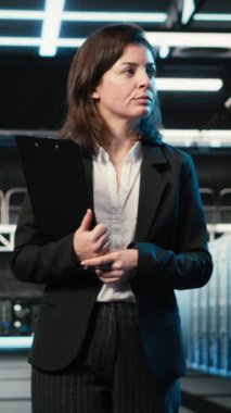 Dikey video denetleme donanımı, mavi kablo örgüleri ve veri merkezinde yönetici. AR veri akışlarına, dijital ikiz simülasyonuna ve sunucu merkezinde yürüyen sistem yöneticisine bakıyorum.