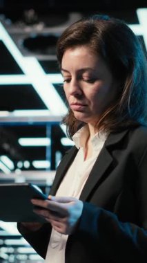 Tablet üzerindeki dikey video veri merkezi programcısı dijital ikiz oluşturmak için ekipman donanımlarını tarıyor. Sunucu merkezindeki kadın teknisyen aygıt, VFX bileşimi, kamera B üzerinde programlama betiği çalıştırıyor