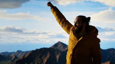 Gururlu kaşif dağın zirvesine ulaşır başarısından memnun ve memnun hisseder, dağların ve gökyüzünün manzaralı arka planından. Kendini geliştirme ve yeni ufuklar. Kamera B.