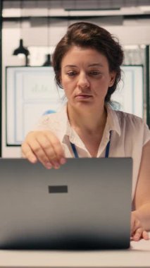 Bilgisayarını açıp masa başında günlük görevleri çözen, analitik üzerinde çalışan ve iş istihbaratını bildiren bir kadının dikey video portresi. Çok uluslu bir şirket ofisinde çalışan profesyonel bir kadın.