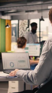 Dikey Video İşletme Profesörü şirket ofisindeki masada tek başına çalışıyor, dizüstü bilgisayardaki çizelgeleri ve grafikleri analiz ediyor. Küresel işletme için performans ölçümleri ve gösterge panelinde öngörü raporları