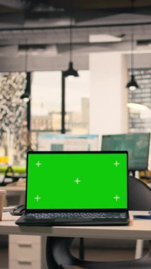 Çalışma istasyonunda dikey video yeşil ekran dizüstü bilgisayar boş, açık ofis, mobilya ve ofis malzemeleriyle modern şirket alanı. Doğal ışık ile rahat çalışma ortamı.