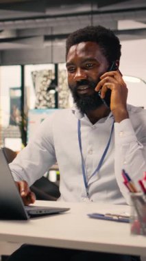 Dikey Video Siyah erkek profesyonel telefonda cep telefonuyla iletişim kuruyor. KPI için iş istihbaratını destekleyen dizüstü bilgisayardaki görsel veriler, grafikler ve grafikler, stratejik