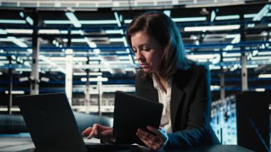 Veri merkezi yazılım geliştiricisi aygıtları kullanarak ekipman donanımlarını optimize ediyor. Sunucu çiftliğindeki kadın dizüstü bilgisayar ve tablette programlama betiği çalıştırıyor, sistem parametrelerini ayarlıyor, kamera A