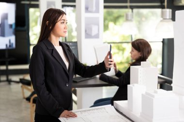 Genç mimar müteahhitlerle iletişim kurmak için cep telefonu kullanır, bina tasarımı hakkında güncelleme sağlar. Masada ölçek modeline sahip kadın tasarımcı, proje ilerlemesini paylaşmak için istemciyle video çağrısına katılır