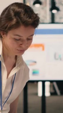 Modern bir ofiste tek başına çalışan bir iş kadınının dikey video portresi bilgisayardaki görsel verileri ve grafikleri analiz ediyor. Performans ölçümlerini ve KPI gösterge panelini gösteren kurumsal çalışma alanı