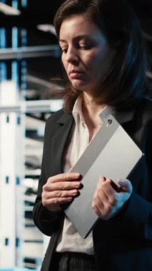 Dikey video otomasyonu, tablet ve mühendis veri merkezinde yürüyor, endüstriyel sistemleri izliyor. IT uzmanı sunucu odası IT profesyoneli ağ donanımı performansını denetlemek için aygıt kullanıyor