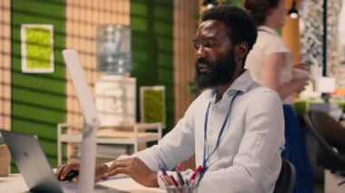 Siyahi bir adam, dizüstü bilgisayarda çalışan profesyonel, çok uluslu bir şirket, kurumsal ofis ortamı. İş zekası, tahmin raporları, üretkenlik, planlama ve kalkınma hedefleri.